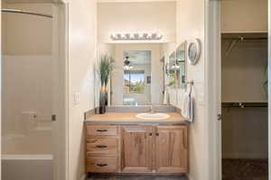 Ensuite bathroom featuring a walk in closet, vanity, ceiling fan, and shower / bath combination