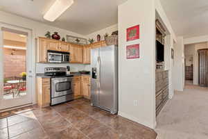 Kitchen with stainless steel appliances, light wood finish cabinetry, dark colored carpet, and dark countertops