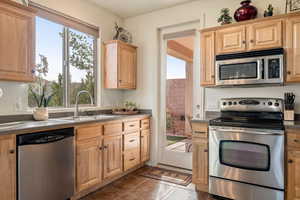 Kitchen with stainless steel appliances, dark countertops, and light wood finish cabinets