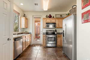 Kitchen with stainless steel appliances, light wood finish cabinets, dark stone finish floors, and dark countertops