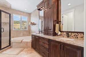 Full bath featuring double vanity, glass enclosed shower, garden tub and travertine floors