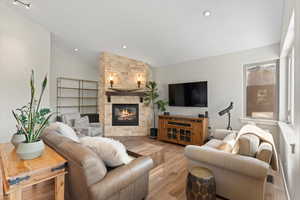Living room featuring a stone fireplace, vaulted ceiling and healthy amount of natural light