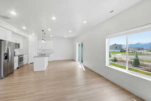 Kitchen with stainless steel appliances, white cabinetry, light wood-style flooring, a mountain view, and a center island with sink