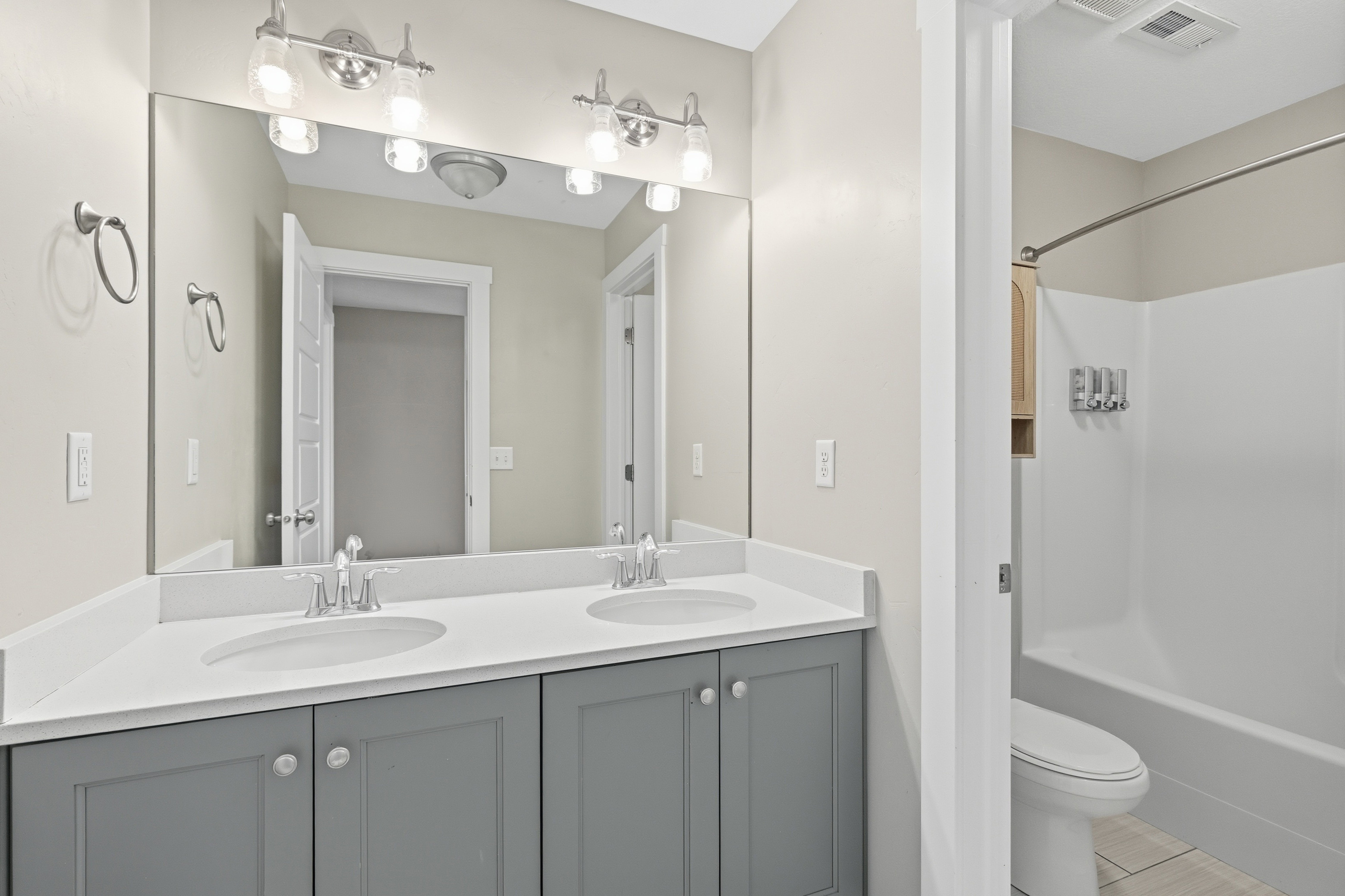 Bathroom featuring a dual vanity with a white countertop and gray cabinetry, brushed nickel hardware, and a large wall-mounted mirror