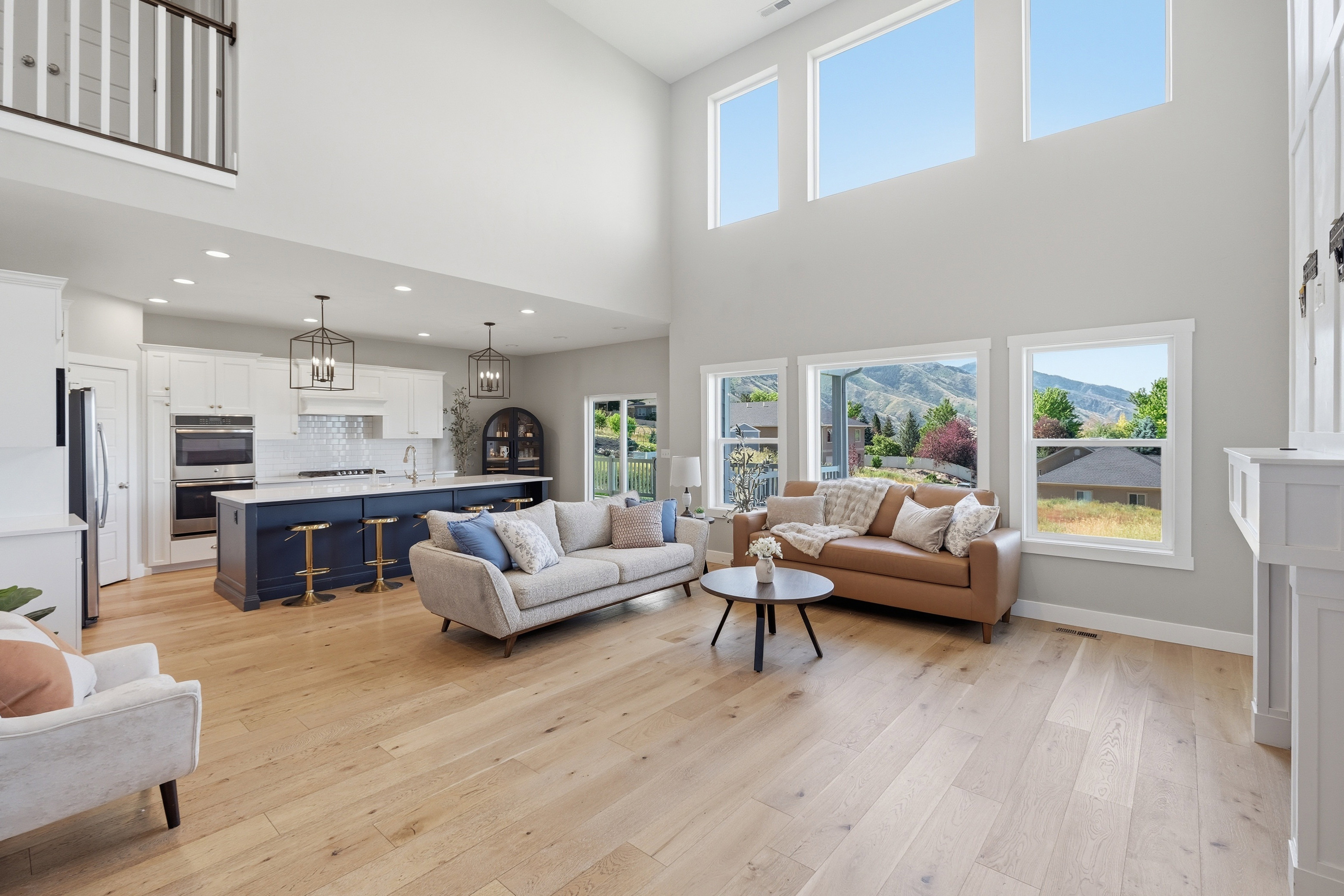 Two-story living area featuring wood-finish flooring, a white fireplace surround, and high ceilings with upper windows