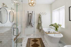 Bathroom featuring a soaking tub, light marble finish floors, and vanity
