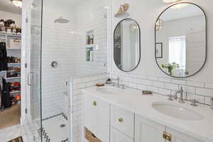 Full bath featuring double vanity, a stall shower, a spacious closet, and tile walls