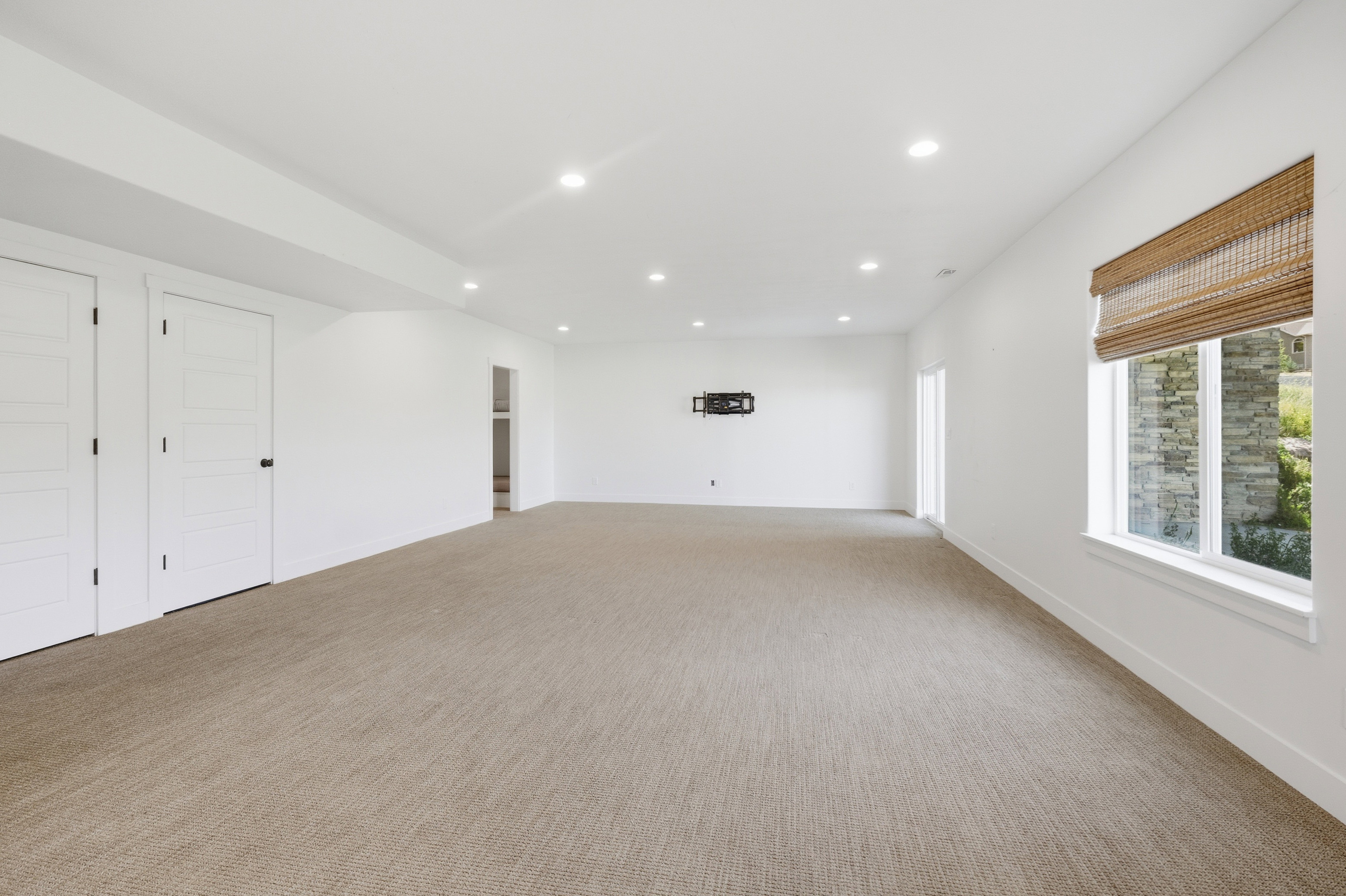 Spacious room featuring neutral carpeting, recessed lighting, white walls, and a window with a natural woven shade