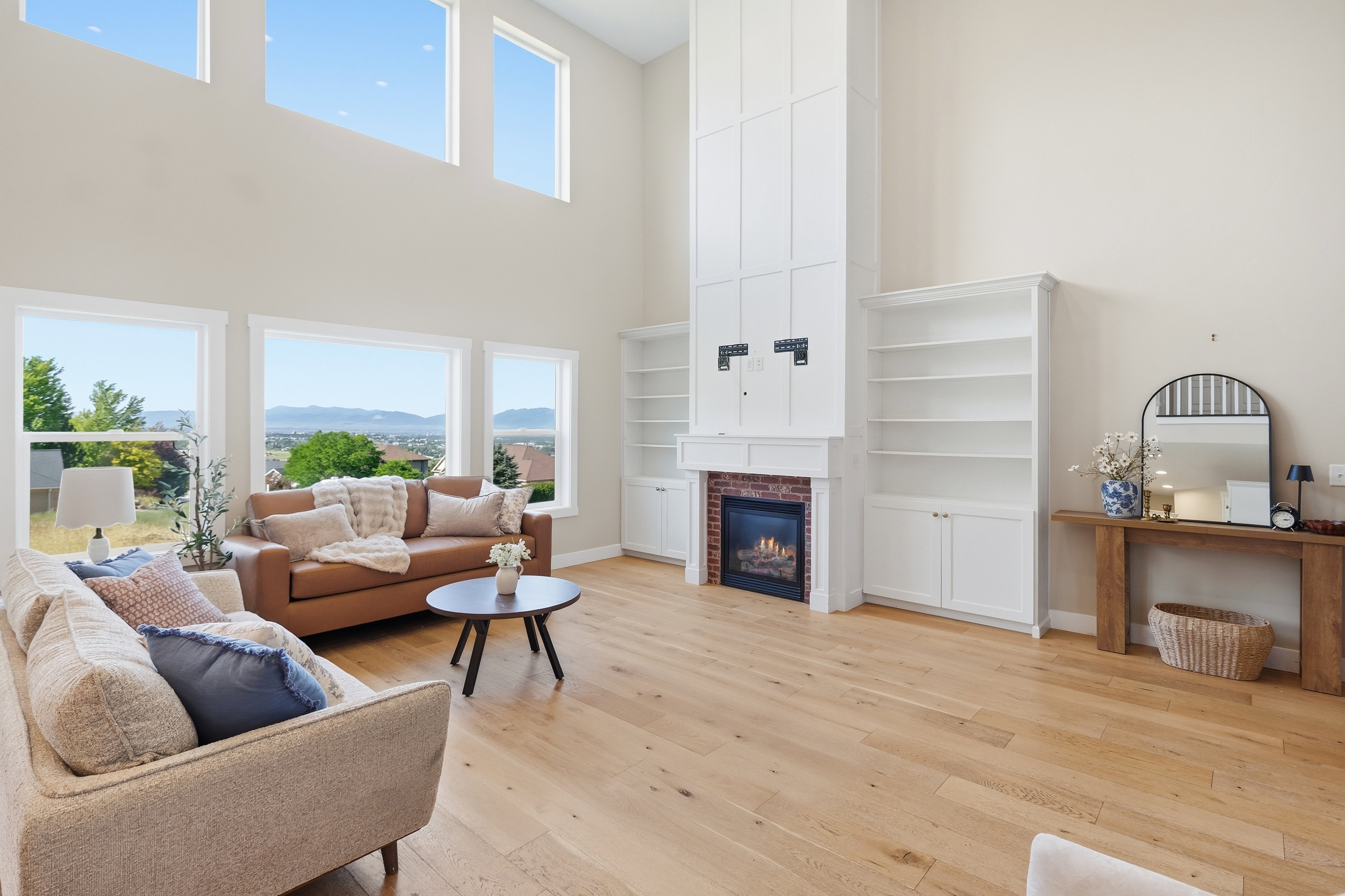 Spacious living area featuring high ceilings, light wood-finish flooring, and a fireplace with a brick surround