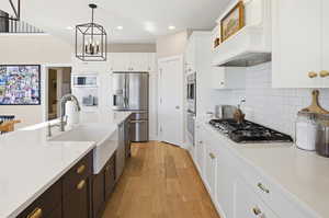 Two tone kitchen featuring dual tone cabinetry, stainless steel appliances, light wood-style floors, light stone countertops, and suspended lighting