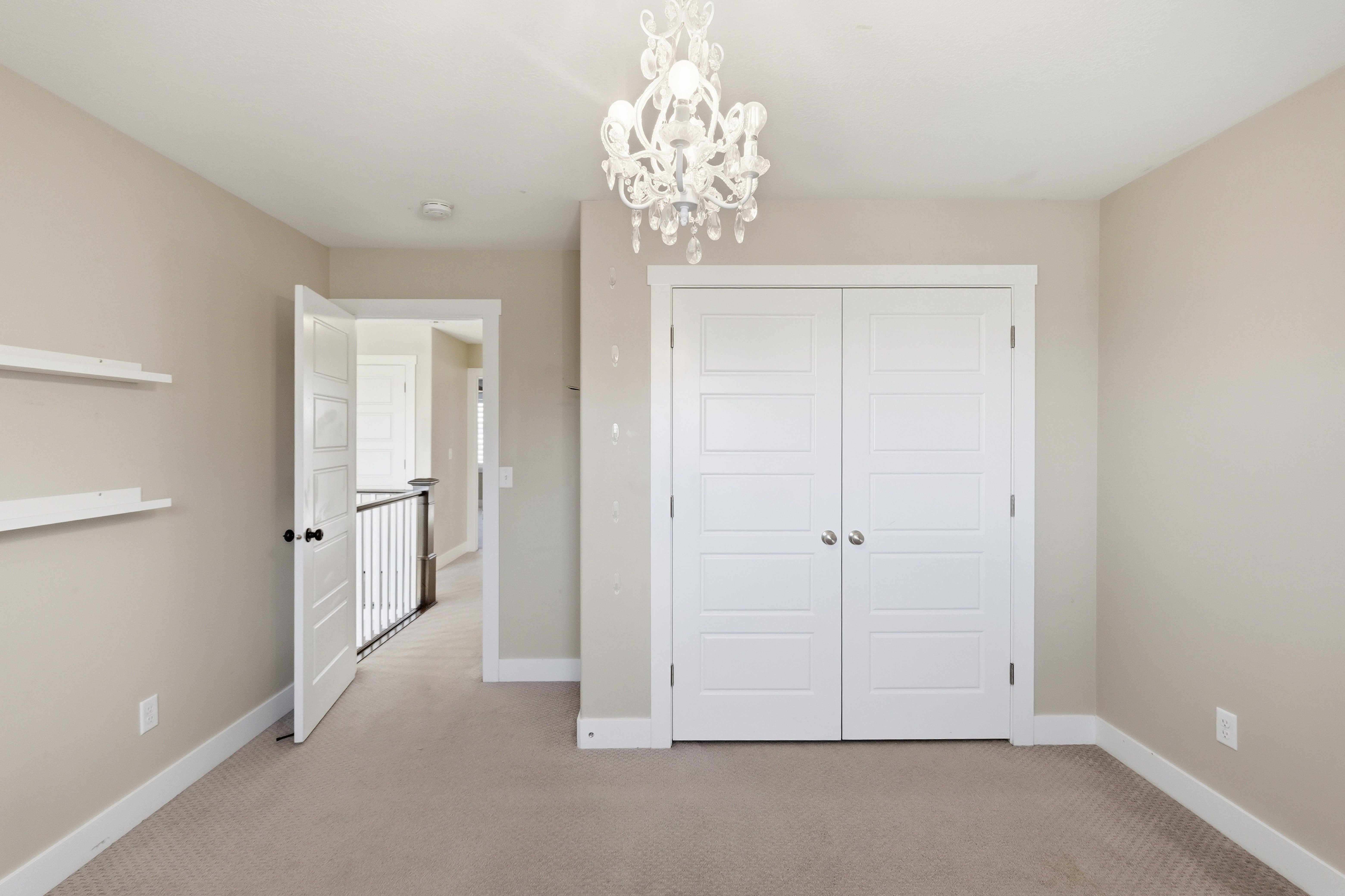 Room featuring plush carpeting, neutral wall tones, a decorative chandelier, white trim, and a double-door closet with modern paneling