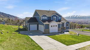 Craftsman inspired home with a mountain view, driveway, a front lawn, a shingled roof, and board and batten siding