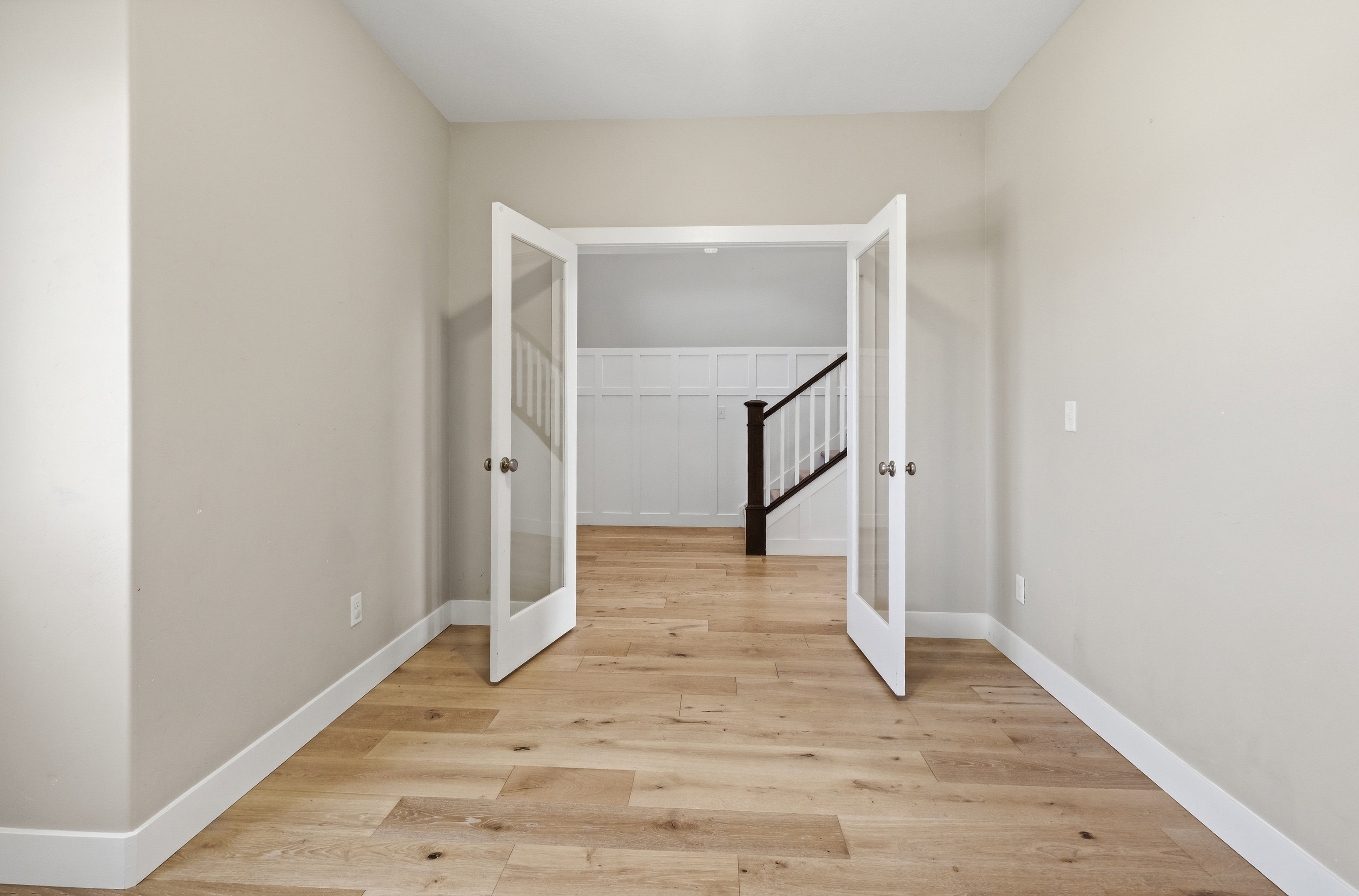 French doors featuring glass panels open to a room with wood-finish flooring, light neutral-toned walls, and white trim