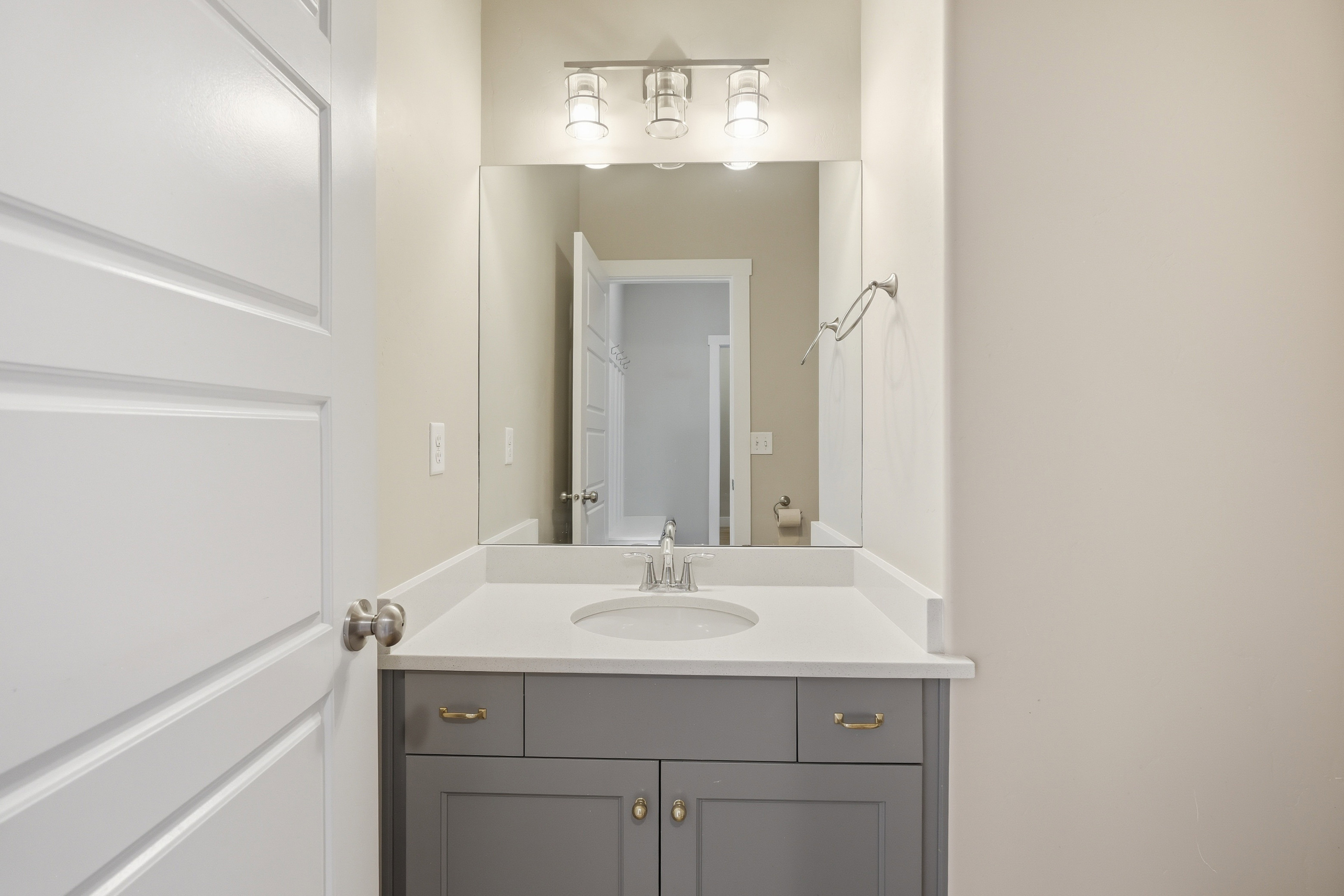 Bathroom vanity featuring a light gray cabinet with gold-toned hardware, an undermount sink, and a white countertop