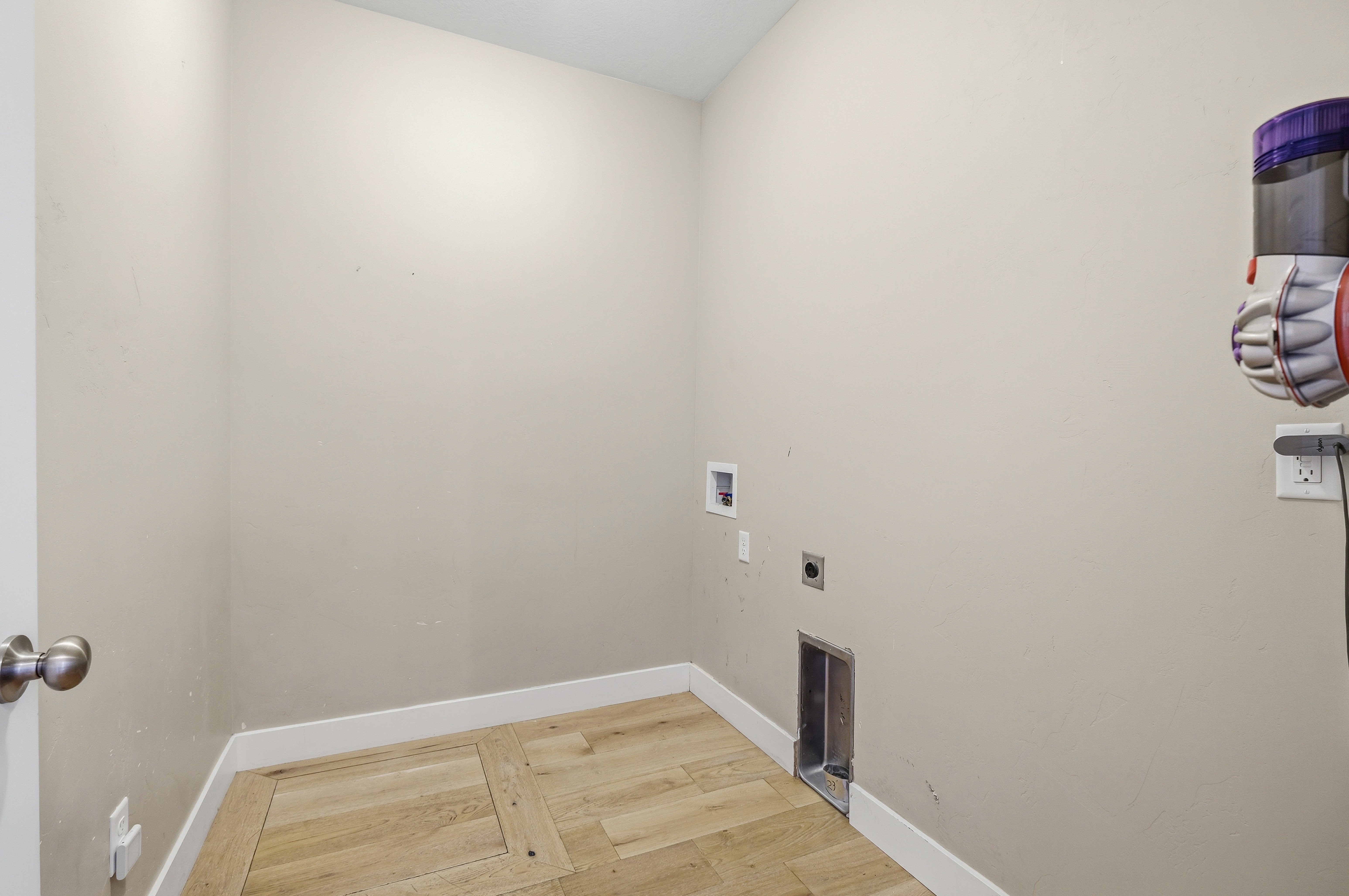 Laundry area with light-toned walls and wood-finish flooring