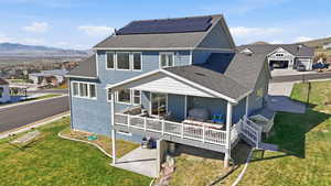 Rear view of property featuring roof with shingles, roof mounted solar panels, a lawn, and a deck with mountain view