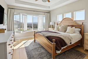 Bedroom featuring a raised ceiling, light wood-type flooring, multiple windows, and ceiling fan