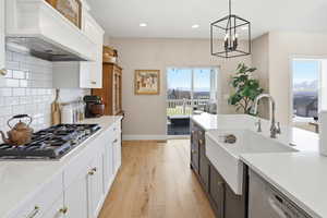 Kitchen featuring two tone cabinetry, stainless steel appliances, light stone countertops, light wood-type flooring, and tasteful backsplash