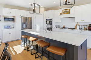 Dual tone kitchen with light wood-type flooring, a kitchen island with sink, dual tone cabinetry, stainless steel appliances, and a kitchen breakfast bar