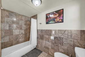 Bathroom featuring tile walls, shower / bath combo, tile patterned flooring, and a wainscoted wall