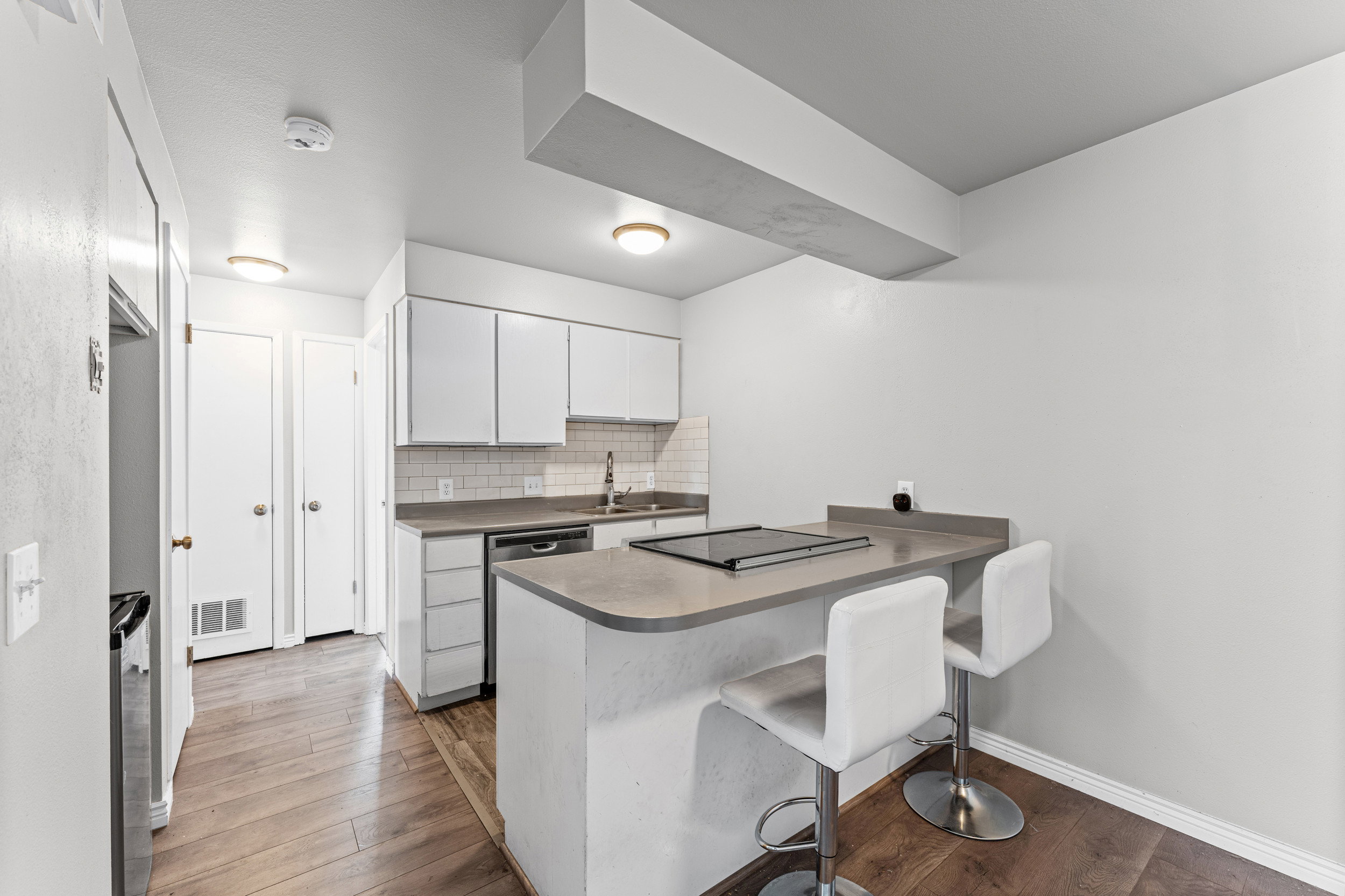 Kitchen featuring a breakfast bar area, a peninsula, white cabinets, backsplash, and dark wood-type flooring