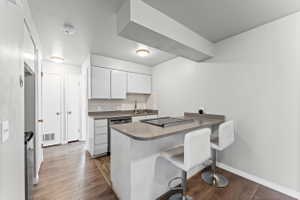 Kitchen featuring a breakfast bar area, a peninsula, white cabinets, backsplash, and dark wood-type flooring