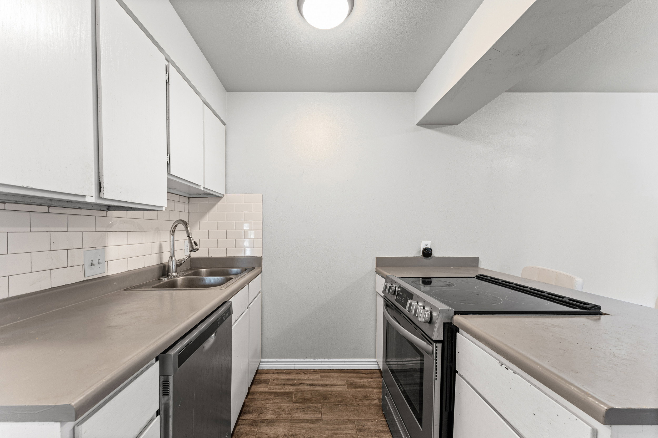Kitchen featuring stainless steel appliances, white cabinetry, dark wood-type flooring, decorative backsplash, and light countertops