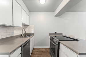 Kitchen featuring stainless steel appliances, white cabinetry, dark wood-type flooring, decorative backsplash, and light countertops
