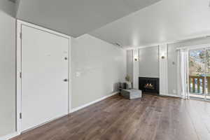 Unfurnished living room featuring a warm lit fireplace and dark wood-style flooring