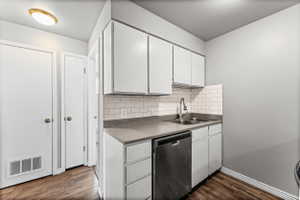 Kitchen with stainless steel dishwasher, decorative backsplash, dark wood-style floors, white cabinets, and light countertops