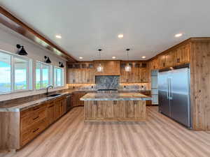 Kitchen featuring stainless steel appliances, a center island, hanging light fixtures, wood finish cabinetry, and tasteful backsplash