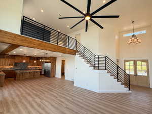 Unfurnished living room featuring suspended lighting, a high ceiling, light wood-type flooring, french doors, and ceiling fan