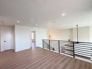 Empty room with light wood-type flooring, hanging lights, and a textured ceiling