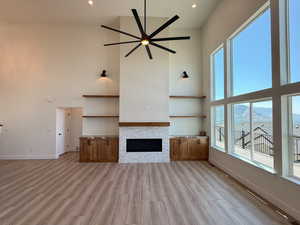 Unfurnished living room with a high ceiling, ceiling fan, a stone fireplace, a mountain view, and light wood-style flooring