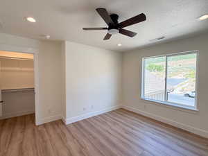 Unfurnished bedroom featuring a walk in closet, recessed lighting, light wood-style flooring, a textured ceiling, and ceiling fan
