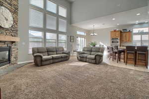 Living area featuring light colored carpet, suspended lighting, plenty of natural light, a stone fireplace, and a high ceiling