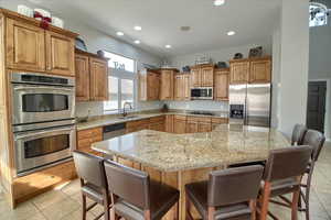 Kitchen with stainless steel appliances, light stone counters, wood finish cabinetry, a kitchen breakfast bar, and recessed lighting