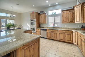 Kitchen featuring wood finish cabinets, a chandelier, stainless steel appliances, light stone counters, and plenty of natural light