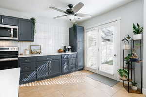 Kitchen featuring decorative backsplash, stainless steel appliances, gray cabinetry, a ceiling fan, and light tile patterned flooring