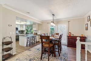 Dining space with dark wood-style flooring, a textured ceiling, and crown molding