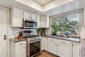 Kitchen with stainless steel appliances, white cabinets, light wood finished floors, decorative backsplash, and dark stone countertops