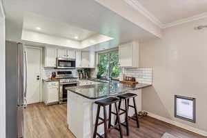 Kitchen with a textured ceiling, white cabinetry, light wood-type flooring, stainless steel appliances, and a tray ceiling
