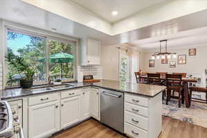 Kitchen with backsplash, light wood-style floors, dishwasher, white cabinetry, and dark stone counters