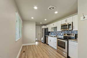 Kitchen with stainless steel appliances, white cabinets, recessed lighting, light wood-style flooring, and light stone countertops