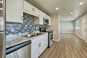 Kitchen featuring stainless steel appliances, white cabinetry, recessed lighting, dark wood-type flooring, and light stone counters