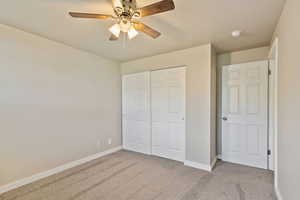 Unfurnished bedroom with light colored carpet, a closet, and a ceiling fan