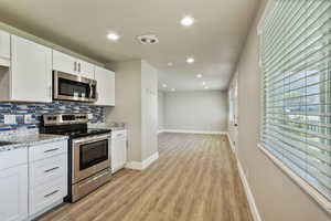 Kitchen with stainless steel appliances, white cabinets, recessed lighting, light stone counters, and tasteful backsplash
