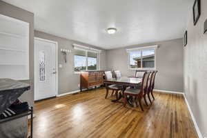 Dining area with a textured wall, built in shelves, light wood finished floors, and a textured ceiling