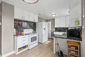 Kitchen with tasteful backsplash, white appliances, open shelves, and white cabinetry