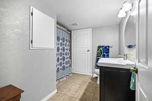 Bathroom with a textured wall, vanity, a textured ceiling, a shower with curtain, and light tile patterned floors
